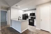 Located at 4350 Jimmy Carter Blvd in Norcross, Georgia, this single-floor unit offers a well-designed layout with a variety of functional and aesthetic features throughout. The living area is a standout space, showcasing dramatic vaulted ceilings that create an open, airy atmosphere. Soft carpeting covers the floor, and a large sliding glass door fitted with vertical blinds floods the room with natural light while providing direct access to an outdoor balcony with views of surrounding greenery. The kitchen is thoughtfully updated, featuring white shaker-style cabinetry, granite-look countertops, a classic white subway tile backsplash, and black appliances including a refrigerator, electric range, and over-the-range microwave. Light wood-look flooring completes the kitchen's clean, modern aesthetic. The bedroom is a comfortable, carpeted space with a textured ceiling, a bright window with horizontal blinds that invite natural light, and a closet with a full-panel door offering generous storage. The bathroom is finished with white tile surrounding the soaking tub and shower combination, wood-look flooring, a large vanity mirror, and clean white fixtures, providing a practical and well-maintained space. Overall, this unit combines functional design with comfortable living spaces suited for everyday life.