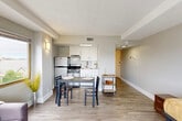 Located at 400 Maynard Street in Ann Arbor, Michigan, this efficiently designed studio-style unit makes the most of its compact footprint through a thoughtful, open-concept layout. The living area is bright and airy, anchored by a striking bank of large corner windows with warm wood-toned frames that flood the space with natural light and offer sweeping views of the Ann Arbor skyline. Light-toned hardwood-style flooring runs throughout, lending a clean, cohesive aesthetic to the entire unit.

The kitchen is neatly integrated along one wall, featuring white cabinetry, a tile backsplash, a stainless steel refrigerator, and a gas range, providing all essential cooking amenities in a streamlined, functional arrangement. A dining area sits adjacent, comfortably accommodating a small table and chairs. The hallway connects the main living space to the bathroom and includes a full-height louvered closet, offering practical storage. The bathroom is well-appointed with a white vanity, a shower-tub combination, and wood-look flooring that complements the rest of the unit.

Neutral gray walls, recessed lighting, and clean white trim throughout create a modern, move-in-ready atmosphere well-suited for urban living in the heart of Ann Arbor.
