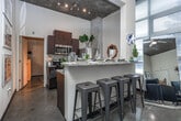 Located at 800 W Marietta St NW in Atlanta's vibrant West Midtown neighborhood, this single-floor loft showcases a bold industrial-chic aesthetic throughout. The open living area commands attention with soaring ceilings, raw exposed concrete walls, and oversized windows that flood the space with natural light and offer leafy outdoor views. The living room provides generous space for seating and entertainment, with the concrete ceiling and columns adding an authentic urban character.

The galley-style kitchen is well-appointed with dark wood cabinetry, granite countertops, stainless steel appliances — including a refrigerator, range, and microwave — and a double sink, all beneath the same dramatic ceiling height.

Two bedrooms each carry their own personality. One features a striking floor-to-ceiling concrete accent wall, a built-in desk, and a walk-in closet. The second bedroom also benefits from natural light through a large window and shares the loft's consistent industrial design language.

Two full bathrooms serve the unit, each featuring a tub-shower combination, a single vanity with dark wood cabinetry, and stone-finish flooring. A hallway with a louvered utility closet and in-unit laundry connections rounds out the practical amenities. Polished concrete floors flow throughout, tying together the cohesive, urban loft atmosphere.