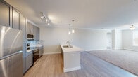 This single-floor residence offers a thoughtfully designed open-concept layout that seamlessly connects the kitchen and living areas. The kitchen is a standout feature, showcasing tall gray shaker-style cabinetry, a mosaic tile backsplash, and a full suite of stainless steel appliances. A large center island with a light quartz countertop and an integrated sink serves as both a functional workspace and a natural gathering point, accented by stylish pendant lighting above. Track lighting and crown molding throughout the main living area add a polished, finished look, while light wood-look flooring grounds the space with warmth and continuity.

The living area is generously proportioned, transitioning from hardwood-style flooring to plush carpeting, creating a comfortable and inviting atmosphere. Bedrooms continue the soft carpet underfoot and feature ceiling fans and natural light from window treatments. A walk-in closet with wire shelving provides practical storage.

The bathroom is well-equipped with a wide vanity featuring blue-gray cabinetry, a white quartz countertop, and a soaking tub with tiled surround. A dedicated in-unit laundry room with full-size washer and dryer adds everyday convenience. Overall, the space presents a clean, modern aesthetic with functional, quality finishes throughout.