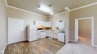 This well-appointed single-floor residence features 3 bedrooms and 2 bathrooms within a thoughtfully designed layout. The kitchen serves as a functional hub, outfitted with white cabinetry, a full suite of white appliances including a refrigerator, electric range, and oven, along with ample counter space and a sink. A stacked washer and dryer unit is conveniently located within the kitchen area, adding everyday practicality. Crown molding accents the kitchen and bedroom ceilings, lending a polished architectural detail throughout the home.

The three bedrooms are carpeted and bathed in natural light through sizable windows fitted with blinds. The generously sized primary bedroom provides a comfortable retreat with notable square footage. Two closets offer organized storage, with wire shelving systems for efficient use of space.

Both bathrooms feature warm hardwood-style flooring, single-sink vanities with storage, and accessibility grab bars. The layout provides direct access to closet space from the bathroom area, enhancing functionality.

Consistent hardwood-style flooring runs through the main living and kitchen areas, while neutral, warm-toned walls create a cohesive and inviting ambiance throughout the home. The overall design balances comfort and utility in a compact, well-organized floor plan.