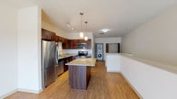 This single-floor residence offers a thoughtfully designed open-concept layout that seamlessly connects the kitchen, dining, and living areas. The kitchen is a standout feature, showcasing rich dark-wood cabinetry, granite countertops, and a full suite of stainless steel appliances, including a refrigerator, electric range, built-in microwave, and dishwasher. A central island with a matching granite surface provides additional prep space and serves as a natural gathering point. Pendant lighting and a track light system illuminate the kitchen, adding a warm, layered ambiance. The adjacent living area is bright and open, with wood-look flooring that runs continuously throughout the main spaces, creating a cohesive and clean aesthetic. A sliding glass door floods the living area with natural light and opens directly onto a private balcony, offering outdoor access. A dedicated in-unit laundry area with a stacked washer and dryer adds everyday convenience. The bathroom continues the refined design language with a dark-wood vanity, granite countertop, tile flooring, and a walk-in shower. Neutral tones and clean lines throughout give the space a modern, move-in-ready feel.