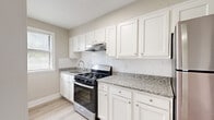 This single-floor home offers four bedrooms, one bathroom, a kitchen, and a hallway, all finished with a clean, modern aesthetic. Light-toned luxury vinyl plank flooring runs throughout, complemented by neutral warm-gray walls and crisp white trim, creating a bright and cohesive look across every room.

The kitchen stands out as a highlight of the home, featuring white shaker-style cabinetry, granite countertops with subtle speckled detailing, a white subway tile backsplash, and stainless steel appliances including a gas range and refrigerator. Natural light filters in through a window, enhancing the kitchen's airy feel.

The four bedrooms are well-proportioned, each finished with the same consistent flooring and neutral palette. The primary bedroom is notably spacious, offering ample room for furnishings. Several bedrooms feature multiple windows fitted with blinds, allowing for excellent natural light and ventilation. Some rooms include closets with panel doors, providing practical storage.

The bathroom is elegantly appointed with floor-to-ceiling marble-look tile surrounding a soaking tub and shower combination, complemented by brushed gold fixtures and a window that brings in natural light.

A connecting hallway ties the layout together efficiently, making the overall flow of the home functional and straightforward.
