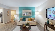 This single-floor residence at 3190 Skinner Mill Rd in Augusta, Georgia, presents a cohesive and well-appointed interior defined by a vibrant teal-and-neutral color palette carried throughout the space. The living room serves as the centerpiece of the home, featuring a bold teal accent wall, wood-look flooring, and ample room for comfortable furnishings. Natural light filters in through large windows dressed with layered blinds and curtains, enhancing the welcoming ambiance. The kitchen is outfitted with crisp white shaker-style cabinetry, granite-look countertops, and black stainless steel appliances including a range, microwave, dishwasher, and refrigerator. A skylight-style overhead fixture brightens the workspace, which connects seamlessly to a dedicated dining area accommodating a round table with seating for four beneath a window overlooking the outdoors. The bedrooms continue the teal design theme, each featuring plush carpet, ceiling fans, multiple windows with outdoor views, and generous natural light. The bathrooms are finished with white cabinetry, granite-look countertops, and wood-look tile flooring. One bathroom features a tub and shower combination with marble-style tile surround, while a second bathroom offers a more compact layout. Overall, the space presents a modern, cohesive aesthetic throughout.