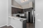 Located at Jefferson Placentia in Placentia, CA, this single-story residence presents a clean, modern aesthetic throughout. The kitchen is a standout feature, boasting rich dark wood cabinetry, a white quartz peninsula countertop, subway tile backsplash, and a full suite of stainless steel appliances including a refrigerator, electric range, and over-the-range microwave. Vaulted ceilings rise above the kitchen area, adding a sense of openness and volume to the space. Wood-look flooring ties the kitchen and entry areas together seamlessly.

The living area is bright and welcoming, with large sliding glass doors dressed in vertical blinds that invite natural light and provide access to an outdoor area. The entry features a transom window above the door, further enhancing the natural light throughout.

The bedrooms are finished with soft wall-to-wall carpeting and neutral tones, offering a calm retreat. One bedroom includes a wide sliding-door closet for ample storage. The bathroom is thoughtfully designed with matching dark wood cabinetry, a long white vanity countertop, large mirrors, and wood-look flooring that continues the cohesive design language of the home, with a separate bathtub visible at the end of the hallway.