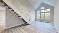 This two-floor space in Manchester, Connecticut is defined by its striking architectural design and modern, freshly updated finishes. The main living area immediately draws attention with its dramatic vaulted ceilings that soar to a cathedral peak, anchored by a large multi-pane window topped with a signature arched transom that floods the room with natural light and views of surrounding greenery. A carpeted staircase with a white balustrade connects the two levels, adding a classic touch to the otherwise contemporary interior.

Light-toned luxury vinyl plank flooring runs consistently throughout both floors, creating a cohesive and clean aesthetic. The kitchen is outfitted with white shaker cabinetry, quartz countertops, a tile backsplash, and stainless steel appliances, offering a functional and polished workspace. The bathroom features elegant marble-style tile surrounding a soaking tub and shower combination, complemented by grey floor tile and white vanity cabinetry.

Bedroom spaces are well-proportioned, with one room offering a walk-in closet and another providing direct access to a private balcony with outdoor views. Additional rooms present flexible layouts suitable for various uses. Throughout, neutral warm-toned walls and abundant natural light contribute to a bright, welcoming ambiance.