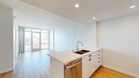 Located at 1150 E Street in San Diego's vibrant East Village, this modern one-bedroom, one-bathroom unit offers a thoughtfully designed open-concept floor plan. Light hardwood flooring flows throughout, complementing the clean white walls and recessed lighting that give the space a bright, contemporary feel.

The combined living, dining, and kitchen area forms the heart of the unit. The kitchen is outfitted with sleek white cabinetry extending to the ceiling, a large quartz waterfall island with a double undermount sink, and a full suite of stainless steel appliances including a French door refrigerator, range, built-in microwave, and dishwasher. A tiled backsplash adds a subtle design accent behind the cooking area.

Floor-to-ceiling windows in both the living area and bedroom flood the space with natural light and frame sweeping views of the San Diego skyline. The bedroom provides direct access to a private balcony, making it an ideal retreat. Three closets offer generous storage throughout the unit.

The bathroom features marble-look tile on both the floors and tub surround, creating a clean, spa-like atmosphere. Additional conveniences include an in-unit laundry area. This unit combines modern finishes, smart storage, and impressive urban views in a prime downtown San Diego location.