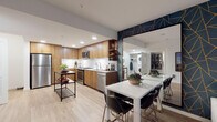 Located at 1146 Harrison Street in Seattle's South Lake Union neighborhood, unit 523 is a thoughtfully designed single-floor residence that balances modern aesthetics with functional living. The open-concept kitchen is a standout feature, showcasing warm walnut-toned cabinetry, white subway tile backsplash, stainless steel appliances including a gas range, dishwasher, and refrigerator, and light hardwood-style flooring that extends throughout the main living areas. A portable kitchen island adds versatility to the space. The dining area accommodates a sleek white table with modern black chairs, seamlessly connecting to the living room. The living room is distinguished by a bold navy and gold geometric accent wall, large windows offering city views, and a cozy seating arrangement. The bedroom continues the sophisticated design language with textured charcoal wallcovering, plush carpet, a ceiling fan, and windows that bring in natural light. In-unit stacked laundry is conveniently tucked away near the kitchen. The bathroom features clean white tile flooring, a wood-toned vanity with an undermount sink, a round mirror with pendant lighting, and a shower-tub combination, delivering a polished, contemporary finish throughout.