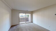 This efficiently designed single-floor unit offers a thoughtful layout across five distinct spaces: a hallway, bedroom, kitchen, dining room, and bathroom. The living and dining area is anchored by a ceiling fan and is finished with neutral carpet, creating a warm, versatile space for everyday living. A sliding glass door fills the room with natural light and provides direct access to an outdoor patio area, framing views of the surrounding greenery. The bedroom is a comfortable, well-proportioned retreat featuring soft carpet flooring, a window with blinds that invites natural light, and clean neutral walls ready for personalization. The kitchen is practically arranged with warm wood cabinetry, granite-look countertops, tile flooring, and full appliances including a refrigerator and dishwasher — offering efficient use of the available space. The bathroom is neatly appointed with a full tub-shower combination, a wood vanity topped with granite-style counters, a mounted sink, and tile flooring throughout. Neutral tones are carried consistently across all rooms, lending the unit a cohesive and move-in-ready aesthetic. A connecting hallway ties all spaces together for easy circulation throughout the home.