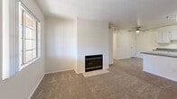 Located at 9901 N Oracle Rd in Oro Valley, Arizona, this three-bedroom, two-bathroom single-floor residence offers a practical and comfortable layout. The open-concept living room and kitchen area serves as the heart of the home, anchored by a wood-burning fireplace set against a clean white accent wall and finished with neutral carpeting. A ceiling fan overhead adds to the relaxed atmosphere. The kitchen is designed in a galley style with ample white cabinetry, grey laminate countertops, light wood-style vinyl flooring, and a full suite of white appliances including a refrigerator, range, microwave, and dishwasher. A pass-through counter connects the kitchen to the living area. The generously sized primary bedroom features plush carpet, a ceiling fan, a sliding glass door opening to a private balcony with outdoor views, and access to a dedicated closet. The additional bedrooms are well-proportioned with carpet flooring and natural light from windows. The bathrooms are clean and functional — one includes a tiled shower with a sleek glass enclosure and modern hardware, while the second features a vanity with grey countertops and convenient in-unit laundry access. A hallway connects the bedrooms, completing the efficient single-level floor plan.
