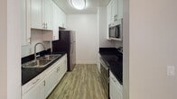Located at 7707 Mission Gorge in San Diego, unit #81 is a well-appointed single-floor residence designed for comfortable, efficient living. The space features durable hardwood-style flooring throughout, complemented by neutral-toned walls and textured ceilings that lend a clean, consistent aesthetic across all rooms.

The galley-style kitchen is a standout feature, offering white shaker cabinetry with brushed nickel hardware, dark granite countertops, a stainless steel sink, and a full suite of stainless steel appliances including a refrigerator, range, and over-the-range microwave. The layout maximizes functionality within the space.

The open living and dining area is bright and welcoming, with a ceiling fan providing year-round comfort. A large sliding glass door floods the room with natural light and provides direct access to a private outdoor patio with greenery views, creating a seamless indoor-outdoor connection. A second living or sleeping area connects via an open corridor, offering flexibility in use.

The bedroom includes a closet with sliding mirror doors, while a separate closet area near the main living space provides additional storage. The bathroom is fitted with a full tub-and-shower combination with brushed nickel fixtures. The unit's single-floor layout ensures easy, step-free navigation throughout the entire space.