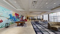 This expansive single-floor hospitality space offers a dynamic and artfully designed environment that seamlessly blends recreation, dining, and social gathering. The space is immediately distinguished by two large-scale, vivid murals — one depicting a colorful underwater and celestial scene, and another showcasing galloping horses and marine life in bold, fantastical strokes — serving as striking focal points throughout the open layout.

The recreational zone features a full-size billiards table set atop a tiled floor area, flanked by plush seating including velvet lounge chairs in deep jewel tones. Adjacent to this is a generously sized lounge area carpeted in a bold plaid pattern, furnished with mixed seating arrangements ideal for both casual gatherings and collaborative use.

A dedicated bar and service area features expansive stone and wood-topped counters with bar-height seating, set against a backdrop of textured tile walls and large windows dressed in sheer white drapery that allow abundant natural light to filter through. A separate café-style counter with pendant globe lighting and a VIVO branded service station adds another layer of hospitality convenience.

The entrance area features a bold cobalt blue architectural element, vibrant pink accent chairs, and verdant potted plants, creating a welcoming and energetic arrival experience. Recessed ceiling lighting and coffered ceiling details complete the polished, contemporary aesthetic throughout.