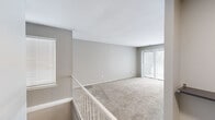 This single-floor home offers a practical and well-appointed layout across three bedrooms, two bathrooms, a kitchen, and two connecting hallways. The living area is finished with neutral-toned wall-to-wall carpeting and light gray walls, creating a clean and cohesive aesthetic throughout. Large vertical blinds and multiple windows allow natural light to fill the space, contributing to an open and airy ambiance. A staircase with a white railing is visible from the main living area, adding a structural focal point to the open room. The kitchen stands out with rich dark-stained wood cabinetry, warm hardwood-style flooring, light granite-look countertops, and white appliances including a gas range and refrigerator — a functional space ideal for everyday cooking. The bedrooms are carpeted and feature neutral gray walls, with the primary bedroom offering dual closets with paneled bi-fold doors, providing generous storage. The secondary bedrooms are well-proportioned with natural window light. Both bathrooms are finished in clean white tile, each equipped with a soaking tub and shower combination. The hallways connect rooms efficiently, maintaining a smooth flow throughout the home. Overall, the space presents a tidy, move-in-ready feel with consistent finishes and practical design.