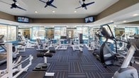 Located at 3600 N Warmbreeze Way in Las Vegas, NV, this single-story amenity space offers a comprehensive fitness and leisure environment designed to support an active lifestyle. The fitness center is a standout feature, outfitted with an extensive array of strength training machines and cardio equipment, including ellipticals and resistance machines. Blue accent walls, large windows overlooking the outdoor pool, ceiling fans, and wall-mounted televisions create a bright, energized atmosphere throughout the gym floor, which is finished with patterned, multi-toned carpet. An adjoining studio room provides a dedicated space for group or individual exercise, featuring hardwood-style flooring, a large wall-mounted television with an interactive fitness display, step platforms, stability balls, and a wall-mounted tablet for guided workouts. Recessed lighting and a tray ceiling give the studio a clean, finished look. Outside, the resort-style pool is the centerpiece of the outdoor space, offering sparkling blue water surrounded by a generous pool deck lined with lounge chairs, private cabanas with curtains, and shade umbrellas. Mature trees frame the space, providing a relaxing, shaded retreat under the Las Vegas sun.