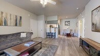 This single-floor residence offers a thoughtfully designed open-concept layout that seamlessly connects the living, dining, and kitchen areas. The living room features light wood-look flooring, a ceiling fan, and a large window that invites natural light and outdoor views, creating a bright and welcoming atmosphere. The kitchen is outfitted with gray cabinetry, white countertops, stainless steel appliances including a gas range, microwave, and dishwasher, and a raised breakfast bar with seating — ideal for casual dining. A dedicated dining area sits adjacent, providing additional space for meals and entertaining. Both bedrooms are carpeted and equipped with ceiling fans, offering a comfortable retreat. The primary bedroom includes sliding glass door access to the outdoors, vaulted ceiling details, and a generously sized walk-in closet with built-in wire shelving for ample storage. The secondary bedroom also features sliding door access. The bathrooms are finished with gray vanity cabinetry, white countertops, and wood-look flooring. A dedicated in-unit laundry room with a full-size washer and dryer adds everyday convenience. Throughout the residence, a neutral color palette and consistent finishes create a cohesive and modern aesthetic.