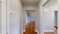 Located at 8402 Greenway Road in Towson, Maryland, this single-floor, 2-bedroom, 1-bathroom home offers a well-organized layout with consistent hardwood flooring flowing throughout every room. The living room is a spacious, open area with warm honey-toned hardwood floors, soft gray walls, and a textured ceiling, creating a neutral and welcoming atmosphere. Two hallways connect the rooms efficiently, lending the home a practical and easy-to-navigate floor plan. The kitchen is equipped with rich warm-toned wood cabinetry, gray laminate countertops, a gas range, and a refrigerator, all set atop light hardwood flooring. A window brings in natural light, giving the kitchen an airy feel. The primary bedroom is a generously sized retreat featuring dual windows that fill the room with natural light and offer views of the surrounding greenery. A second closet set adds notable storage. The second bedroom is a comfortable, light-filled room with its own window. The full bathroom is thoughtfully finished with white subway tile surrounding the bathtub, a granite-topped vanity with an undermount sink, wood-look flooring, and a window for natural ventilation and light. White trim and baseboards are consistent throughout, tying the home's clean, classic aesthetic together.