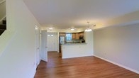 This two-floor residence offers a thoughtfully designed layout that balances comfort and functionality. The main level showcases an open-concept living and kitchen area, where warm hardwood-style flooring flows seamlessly throughout the space, creating a cohesive and inviting atmosphere.

The kitchen is a standout feature, outfitted with stainless steel appliances — including a refrigerator and microwave — light wood cabinetry, and granite-style countertops. A peninsula counter extends into the living area, offering additional prep space and serving as a natural divider between the kitchen and the open living room. A pendant chandelier adds a decorative touch above the peninsula, complementing the flush-mount ceiling lighting found throughout the main level.

Natural light filters in through a window above the kitchen sink, brightening the space and offering a view of the surrounding greenery. A secondary entry door with sidelight glass panels provides additional natural light near the hallway, which leads to additional rooms beyond. The clean white walls and neutral tones throughout create a bright, airy ambiance well-suited for everyday living.

With two floors of living space, this residence provides ample room for a variety of lifestyle needs, combining practical design with comfortable, welcoming interiors.