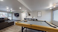 Located at 526 W Hale St in Boise, Idaho, this single-floor space is thoughtfully designed for community use, social gatherings, and recreational activities. The layout is open and functional, with distinct zones that flow naturally into one another across light wood-look flooring that runs throughout.

The game room is a standout feature, anchored by a full-size pool table with a wood frame and gray felt surface. A wall-mounted flat-screen television and built-in storage with gray cabinetry complete the area, which is decorated with Idaho-themed wall art and a Boise city map print, adding a locally inspired touch.

Adjacent to the game room, a well-equipped kitchenette features gray cabinetry, white countertops, open shelving stocked with supplies, a sink, and small appliances. A skylight overhead enhances the brightness of the space, which opens visually toward a large window overlooking the parking area.

The dining area is defined by a white-painted cinder block accent wall and a generous window that brings in natural light and outdoor views. A wood dining table with cross-back chairs comfortably accommodates a small group.

Two lounge areas each feature large sectional sofas in charcoal gray, oversized ottomans, and sizable windows with outdoor views, creating a comfortable, relaxed atmosphere throughout.