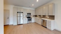 This well-appointed single-floor residence offers a thoughtfully designed open-concept layout that seamlessly connects the kitchen, dining, and living areas. The kitchen is a functional centerpiece, featuring stainless steel appliances — including a refrigerator, range, microwave, and dishwasher — complemented by crisp white shaker-style cabinetry, a tile backsplash, and light hardwood-style flooring that extends throughout the main living spaces. The living area is bright and airy, highlighted by a ceiling fan and large sliding glass doors that open to a private balcony with an outdoor view, allowing abundant natural light to fill the room. The bedrooms are finished with plush carpeting, ceiling fans, and window blinds that provide privacy while still admitting natural light. The bathroom features clean white cabinetry with modern hardware, a glass-enclosed shower, and light wood-style flooring that ties in with the rest of the home. Storage is well addressed throughout, including a spacious walk-in closet outfitted with wire shelving. An in-unit washer and dryer area adds further convenience. The overall design palette of neutral tones and contemporary finishes creates a clean, modern ambiance throughout.