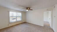 Located at 2438 Whitmire Blvd in Midland, Texas, this single-story residence offers a straightforward and functional layout designed for comfortable everyday living. Throughout the home, rooms are finished with neutral-toned carpet and cream-colored walls, creating a clean and cohesive aesthetic. Each room is equipped with a ceiling fan fitted with a light fixture, contributing to both air circulation and ambient lighting.

The living area is generously proportioned, featuring a large window dressed with vertical blinds that allow natural light to filter in while offering a view of the surrounding exterior. A textured ceiling adds a classic residential touch consistent throughout the home.

The kitchen is well-appointed with rich, dark wood cabinetry providing ample storage, granite-look countertops, a double-basin stainless steel sink, and white appliances including an electric range, over-the-range microwave, and refrigerator. The kitchen flooring transitions to a light wood-look surface, distinguishing it from the carpeted living spaces.

The bedrooms are comfortably sized, each featuring carpet flooring, vertical blind-covered windows that bring in natural light, and ceiling fans. The bathroom includes a full tub-shower combination with classic white tile surround, a toilet, and overhead ventilation, maintaining a clean and utilitarian design.
