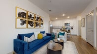 This single-floor residence features a well-designed open-concept layout that seamlessly connects the living, dining, and kitchen areas. The living room is anchored by smooth white walls and wood-look flooring, creating a clean, contemporary backdrop. Recessed lighting illuminates the space efficiently throughout.

The kitchen is well-appointed with stainless steel appliances, including a refrigerator, range, microwave, and dishwasher. Crisp white shaker-style cabinetry extends to the upper walls, providing generous storage, while granite countertops add a refined finish. A dedicated dining area adjacent to the kitchen accommodates a round table with seating.

The bedroom is carpeted for comfort and features a large window that admits substantial natural light while offering exterior views. The room provides a calm, restful atmosphere complemented by neutral tones.

The bathroom includes a full tub-shower combination with tiled surround, a white vanity with countertop storage, and wood-look flooring that ties cohesively to the rest of the unit. Overall, the space presents a modern, functional design with consistent finishes across all rooms.