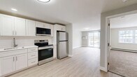 This well-appointed one-bedroom, one-bathroom unit at 144 Dunbarton Rd in Manchester, New Hampshire offers a clean, modern aesthetic throughout its efficiently designed layout. The kitchen is a standout feature, showcasing white shaker-style cabinetry, a classic subway tile backsplash, white quartz countertops, and a full suite of stainless steel appliances including a range, over-the-range microwave, dishwasher, and refrigerator. Light wood-style luxury flooring runs through the kitchen and living areas, lending a bright, cohesive feel to the open-plan space. The living room is bathed in natural light and opens directly to an outdoor balcony through a sliding glass door, offering pleasant outdoor views. A wall-mounted air conditioning unit and baseboard heating ensure year-round comfort. The bedroom is carpeted for warmth and comfort, featuring a window that brings in natural light. The bathroom is finished with a full tub-and-shower combination, brushed gold fixtures, and wood-style flooring. Throughout the unit, neutral wall tones and clean white trim create a calm, move-in-ready atmosphere suited for comfortable everyday living.