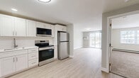 This well-appointed one-bedroom, one-bathroom unit at 144 Dunbarton Rd in Manchester, New Hampshire offers a clean, modern aesthetic throughout its efficiently designed layout. The kitchen is a standout feature, showcasing white shaker-style cabinetry, a classic subway tile backsplash, white quartz countertops, and a full suite of stainless steel appliances including a range, over-the-range microwave, dishwasher, and refrigerator. Light wood-style luxury flooring runs through the kitchen and living areas, lending a bright, cohesive feel to the open-plan space. The living room is bathed in natural light and opens directly to an outdoor balcony through a sliding glass door, offering pleasant outdoor views. A wall-mounted air conditioning unit and baseboard heating ensure year-round comfort. The bedroom is carpeted for warmth and comfort, featuring a window that brings in natural light. The bathroom is finished with a full tub-and-shower combination, brushed gold fixtures, and wood-style flooring. Throughout the unit, neutral wall tones and clean white trim create a calm, move-in-ready atmosphere suited for comfortable everyday living.