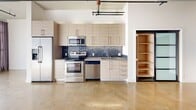 Located at 819 Santee St in the heart of Downtown Los Angeles, this contemporary urban loft offers a thoughtfully designed single-floor layout with an industrial-modern aesthetic. Polished concrete floors extend throughout the open living area, complemented by crisp white walls, exposed ceiling pipes, and track lighting that highlight the loft's architectural character. Large windows dressed with soft curtains allow natural light to fill the space, creating a bright and airy atmosphere.

The kitchen is well-appointed with light wood cabinetry, stainless steel appliances including a refrigerator, range, over-the-range microwave, and dishwasher, along with a striking blue mosaic tile backsplash and ample counter space. An adjacent open shelving unit adds practical storage.

The bathroom is finished to a high standard, featuring large-format gray floor tiles, a glass-enclosed shower and tub combination adorned with dark stacked stone tile, and clean white fixtures. A stacked washer and dryer unit is conveniently integrated into the bathroom area, adding in-unit laundry functionality. The overall design balances industrial elements with modern finishes, making this Downtown LA loft a functional and stylish urban retreat.