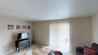 This single-story residence located at 5301 S East St in Indianapolis, Indiana, offers a well-organized layout across several functional living spaces. The living room serves as the central gathering area, featuring soft carpeting, neutral-toned walls, and a large sliding glass door fitted with vertical blinds that allows natural light to filter in while providing access to an outdoor space. The open, clean-lined design creates a welcoming and comfortable atmosphere.

Adjacent to the living area, the dining space accommodates a small table and chairs beneath a ceiling fan with integrated lighting, making it a practical area for everyday meals. The kitchen is generously proportioned, featuring warm wood cabinetry lining both sides of the galley-style layout, white countertops, tile flooring, a built-in oven, coil-top range, and a full-size refrigerator, along with open shelving for additional storage.

The bedrooms are carpeted and restful in character, each offering windows that bring in natural light. The bathrooms are finished with tile flooring and feature a tub-shower combination, a wide vanity with ample counter space, and a large mirror, providing a clean and functional design throughout.