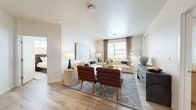 Located at 7501 Jefferson St NE in Albuquerque, New Mexico, this two-bedroom, two-bathroom residence offers a thoughtfully designed single-floor layout that balances comfort and modern style. The heart of the home is a bright, open-concept kitchen and living area, where wood-style plank flooring flows seamlessly throughout. The kitchen features sleek gray cabinetry, stainless steel appliances including a French door refrigerator, and a quartz-topped island with bar seating — ideal for both cooking and entertaining. The spacious living area is bathed in natural light from large windows dressed with elegant drapes, creating a warm and inviting atmosphere. Both bedrooms are generously sized, with the primary bedroom offering a well-organized walk-in closet with built-in shelving. The primary bathroom is appointed with dual sinks, gray vanity cabinetry, quartz countertops, and a glass-enclosed shower. The second bathroom features a full soaking tub with tiled surround and a matching gray vanity. A private balcony with composite wood decking and stucco walls provides outdoor views of the surrounding Albuquerque neighborhood. Additional conveniences include in-unit laundry and ample closet storage throughout.