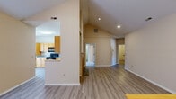 This single-floor home is defined by its striking vaulted ceilings, which rise dramatically over the open-concept living and dining areas, creating an airy, spacious atmosphere. Light-toned walls and wood-look flooring run throughout the main living spaces, contributing to a clean, cohesive aesthetic.

The kitchen is well-appointed with warm honey-toned cabinetry, granite-look countertops, black appliances including a range, microwave, and dishwasher, and a peninsula that opens toward the main living area. A bay window area provides natural light and additional visual interest.

The living room features soaring vaulted ceilings, French doors that open to an outdoor space, and a built-in shelving and cabinetry unit — a practical and decorative focal point. Recessed lighting supplements the natural light throughout.

The bedrooms are carpeted and finished in neutral tones, offering a comfortable, quiet retreat. One bedroom includes access to a walk-in closet. The bathrooms are consistent in style, each featuring tile-surround tub-shower combinations, wood-toned vanity cabinetry, and wood-look flooring. A second full bathroom includes a soaking tub with full tile surround. Overall, the home presents a functional and well-organized layout with cohesive finishes throughout.