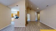 This single-floor home is defined by its striking vaulted ceilings, which rise dramatically over the open-concept living and dining areas, creating an airy, spacious atmosphere. Light-toned walls and wood-look flooring run throughout the main living spaces, contributing to a clean, cohesive aesthetic.

The kitchen is well-appointed with warm honey-toned cabinetry, granite-look countertops, black appliances including a range, microwave, and dishwasher, and a peninsula that opens toward the main living area. A bay window area provides natural light and additional visual interest.

The living room features soaring vaulted ceilings, French doors that open to an outdoor space, and a built-in shelving and cabinetry unit — a practical and decorative focal point. Recessed lighting supplements the natural light throughout.

The bedrooms are carpeted and finished in neutral tones, offering a comfortable, quiet retreat. One bedroom includes access to a walk-in closet. The bathrooms are consistent in style, each featuring tile-surround tub-shower combinations, wood-toned vanity cabinetry, and wood-look flooring. A second full bathroom includes a soaking tub with full tile surround. Overall, the home presents a functional and well-organized layout with cohesive finishes throughout.