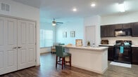 Located at 5215 S Raul Longoria Rd in Edinburg, Texas, this single-floor residence offers a thoughtfully designed open-concept layout that seamlessly connects the kitchen, dining, and living areas. The kitchen is a standout feature, boasting dark espresso cabinetry, light countertops, a center island with a built-in sink and breakfast bar seating, and black appliances including a range, microwave, and refrigerator. Recessed lighting and wood-look plank flooring throughout the main living area add a clean, modern aesthetic.

The living area is bright and inviting, benefiting from large windows that allow ample natural light to fill the space, complemented by a ceiling fan overhead. A dedicated sitting nook provides a cozy retreat with its own window view. The bedrooms feature plush carpeting, ceiling fans, and generous closet space, offering a comfortable and quiet environment. The bathroom includes dark cabinetry for storage, consistent with the design language found throughout the unit.

White walls and clean architectural lines give the interior a fresh, neutral backdrop, while wood-look flooring creates a warm contrast. The overall ambiance is modern, functional, and well-lit, making this a practical and attractive living space in the heart of Edinburg, TX.