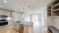 Located at 3550 N A W Grimes Blvd in Round Rock, TX, this thoughtfully designed 2-bedroom, 2-bathroom residence offers a clean, contemporary aesthetic throughout its single-floor layout. The open-concept kitchen and living area serves as the heart of the home, featuring light hardwood-style flooring, crisp white shaker cabinetry extending to the ceiling, granite countertops, a large center island with a undermount sink, and a full suite of stainless steel appliances including a refrigerator, range, microwave, and dishwasher. Stylish pendant lighting illuminates the island and flows seamlessly into the living area, which is fitted with a ceiling fan and anchored by a large sliding glass door leading to a private balcony with open outdoor views. A built-in mudroom-style storage unit near the entry provides shelving, hooks, and a granite-topped bench for added functionality. Both bedrooms are carpeted and generously sized, with the primary bedroom offering walk-in closet access. The bathrooms are well-appointed, with one featuring a tiled tub-shower combination. Two dedicated closets provide ample storage throughout. The unit presents a bright, neutral palette ideal for a variety of living styles.