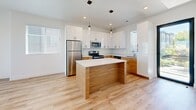Located at 527 40th St in South Ogden, Utah, this contemporary three-story home offers a clean, modern aesthetic with thoughtfully designed living spaces across each level. The entry level provides a welcoming entrance with staircase access to the main living floor above.

The main floor hosts an open-concept kitchen and living area bathed in natural light from multiple windows. The kitchen is a standout feature, showcasing two-tone cabinetry with warm wood lower cabinets and crisp white uppers, white quartz countertops, a central island with pendant lighting, and stainless steel appliances. Light hardwood-style flooring flows throughout this level, complementing the bright, white walls and creating an airy, cohesive feel.

The upper floor contains both bedrooms, including a spacious primary bedroom with soaring ceilings, oversized windows with transom glass above, and plush carpeting. The second bedroom also features generous windows with outdoor views and direct access to an en-suite bathroom. Four bathrooms throughout the home are finished with warm wood vanities, white quartz countertops, large mirrors, and light tile flooring — with some featuring a full tub-shower combination. A hallway, closet, and multiple staircases ensure practical connectivity across all three floors.