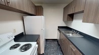 This single-floor unit offers a practical and functional layout designed to maximize comfort and usability. The galley-style kitchen is well-appointed with medium-toned wood laminate cabinetry lining both walls, complemented by dark countertops and a stainless steel sink. White appliances, including a coil-burner range and a full-size refrigerator, complete the kitchen's essentials, while overhead cabinetry provides ample storage throughout.

The living room is a bright, open space featuring plush wall-to-wall carpeting and a ceiling fan with an integrated light fixture. A set of full-height sliding glass doors dressed with vertical blinds allows generous natural light to fill the room and opens the space visually. Clean white walls create a neutral backdrop adaptable to a variety of décor styles.

The bedroom is a well-sized, carpeted room with neutral white walls, a window dressed with horizontal blinds, and convenient access to adjacent spaces. The bathroom is finished in a classic all-white palette, featuring small mosaic tile flooring, a white vanity with under-sink cabinetry, a medicine cabinet mirror, and standard fixtures. The overall design of the unit is clean and move-in ready, with consistent finishes throughout that give the space a cohesive, understated character.