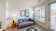 This thoughtfully designed single-floor residence showcases a cohesive modern aesthetic with clean lines and contemporary finishes throughout. The kitchen is a standout feature, outfitted with dark wood-grain cabinetry, light quartz countertops, a classic white subway tile backsplash, and a full suite of stainless steel appliances, including a range, over-the-range microwave, refrigerator, and dishwasher. Light wood-style flooring runs through the kitchen and connects seamlessly to the rest of the common areas.

The living room is bright and welcoming, featuring large windows fitted with horizontal blinds that fill the space with natural light. A glass-panel door provides direct access to an outdoor area, enhancing the sense of openness. Wood-style flooring continues through this space, complementing the room's warm, modern character.

Two carpeted bedrooms offer comfortable retreats, each equipped with a ceiling fan and ample natural light from generously sized windows. The bedrooms feature neutral tones and clean white walls that create a calm, restful ambiance.

The bathroom maintains the same contemporary design language, with a dark-wood vanity, white quartz countertop, a large wall mirror, wood-style flooring, and a tiled shower-tub combination. The overall design of this residence is unified, modern, and functional.