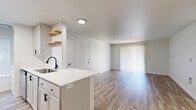 Located at 8364 SW Pfaffle St in Tigard, Oregon, this single-floor 2-bedroom, 2-bathroom residence offers a clean, contemporary design throughout. The open-concept living and dining area is anchored by light wood-style plank flooring that runs continuously through the space, complemented by neutral white walls that maximize brightness. A large sliding glass door fitted with vertical blinds floods the living area with natural light and provides access to the outdoors.

The galley-style kitchen is thoughtfully appointed with white shaker cabinetry accented by matte black hardware, white quartz countertops, a subway tile backsplash, and stainless steel appliances including a refrigerator, range, and dishwasher. A peninsula with an undermount sink and open wood floating shelves adds both function and style to the kitchen layout.

Each bedroom is well-proportioned, offering ample space and natural light through window blinds that frame views of surrounding greenery. One bedroom features a wide sliding-door closet, providing generous storage. Baseboard heating units are present in the bedrooms, ensuring year-round comfort.

The unit's overall aesthetic is modern and move-in ready, with a bright, airy ambiance created by the consistent use of light tones, updated finishes, and an efficiently designed single-level floor plan.
