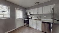 Located at 4111 N Poplar Ave in Tampa, Florida, this single-floor unit offers a clean, modern interior with a consistent design palette throughout. The space is finished with light-toned vinyl plank flooring that runs through the main living areas and bedrooms, complemented by neutral gray walls and crisp white trim.

The kitchen is well-appointed with white shaker-style cabinetry featuring brushed nickel hardware, light countertops, and a full suite of stainless steel appliances including a range, over-the-range microwave, dishwasher, and refrigerator. A stainless steel sink with a gooseneck faucet anchors the workspace, and a door with a windowed blind provides direct exterior access and natural light.

The living area is open and generously sized, with blinds-covered windows that allow natural light to fill the room. Bedrooms are well-proportioned, each featuring the same wood-look flooring and neutral tones, offering a clean and versatile backdrop.

The bathrooms reflect the same updated aesthetic. One features a white vanity with a vessel sink, wall sconce lighting, and tiled walls, while a second full bathroom includes a tub/shower combo with white tile surround and a window for ventilation. The overall layout, visible in the dollhouse view, offers a functional and efficient flow between all areas of the home.