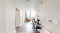 Located at 112 Market St in downtown Harrisburg, PA, this well-appointed one-bedroom, one-bathroom residence offers a thoughtfully designed single-floor layout. The entryway hallway sets an elegant tone, featuring wood-look flooring, crisp white walls, and a stylish console area that leads the eye toward the bright, window-lined living space beyond. The living room is bathed in natural light from large floor-to-ceiling windows that frame sweeping views of the Susquehanna River and the historic Market Street Bridge, creating a striking focal point. The combined dining and kitchen area is both functional and refined, showcasing white shaker cabinetry, dark granite countertops, a classic subway-tile backsplash, and a full suite of stainless steel appliances. A dining nook with a light wood table sits comfortably alongside the kitchen. The bedroom continues the airy aesthetic with plush carpeting, a generous double-door closet, and expansive windows offering the same breathtaking river views. The bathroom features warm wood-look flooring, white cabinetry with ample storage, and a marble-surround tub and shower. A dedicated laundry area and two closets add practical convenience to this polished urban residence.