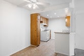 Located at 200 South Citron Street in Anaheim, California, this single-floor residence offers two bedrooms and two bathrooms within a thoughtfully arranged floor plan. The kitchen is a functional highlight, featuring warm wood cabinetry that extends from floor to ceiling, light granite-style countertops, a white gas range, a built-in dishwasher, and a double-basin sink. A peninsula counter with pendant lighting separates the kitchen from the living area, creating an open, connected feel. Recessed lighting and a ceiling fan add comfort and practicality to the shared living space, which is finished with durable tile flooring. The bedrooms are carpeted for warmth and comfort, each featuring clean white walls and closets with double hanging rods for ample storage. Windows in the bedrooms allow natural light to filter in, lending a bright and airy quality to the rooms. The bathrooms are finished with matching wood vanities topped with light countertops, tile flooring, and a full tub-shower combination with chrome fixtures. The overall aesthetic is clean and functional, with a consistent use of warm wood tones and neutral finishes throughout the space.