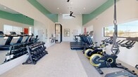 Located at 450 N Apache Rd in Buckeye, Arizona, this fitness center is a thoughtfully designed exercise room that delivers a comprehensive workout experience. The space features soaring vaulted ceilings accented with a fresh sage green color band, crisp white walls, and light-toned carpet flooring, creating a clean and energizing atmosphere throughout. Ceiling fans and recessed lighting ensure the room remains comfortable and well-lit during any workout.

Natural light pours in through large sliding glass doors and multiple windows, offering views of the surrounding neighborhood and bringing an open, airy feel to the interior. The cardio zone is anchored by a row of commercial-grade treadmills and stationary upright bikes, while a dedicated cycling area houses several Hoist spin bikes alongside a multi-functional strength training rack stocked with a variety of weighted accessories. A full dumbbell rack lines one wall, paired with a large mirror that enhances the sense of space. A dual-station drinking fountain is conveniently mounted along the wall, and motivational artwork adds a welcoming, community-oriented character. An adjacent glassed-in room provides additional functional space. This fitness center offers a complete range of equipment to support cardio, strength, and cycling training needs.
