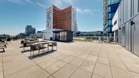 Located at 742 Rue William in Montréal's dynamic Griffin Town neighbourhood, this rooftop terrace offers a generously proportioned outdoor amenity space with sweeping panoramic views of the surrounding cityscape. The terrace is finished with large-format porcelain pavers throughout, lending a clean, contemporary aesthetic to the entire level.

The main open-air section is expansive and sun-drenched, accommodating multiple seating and dining configurations, including picnic-style tables with benches, bistro table sets, and casual lounge chairs — ideal for both social gatherings and relaxed outdoor enjoyment. A compact, glass-fronted pavilion structure anchors one end of the terrace, providing a sheltered focal point and additional functionality.

A covered outdoor alcove with a white panel ceiling and modern railing offers a partially shaded retreat, furnished with lounge chairs and a side table for intimate seating. Elsewhere, a charming covered nook with a rustic wood-beamed ceiling and painted wood decking provides a warmer, more sheltered corner with its own seating.

The perimeter is lined with sleek metal railings that preserve unobstructed sightlines across the Montréal skyline. Abundant natural light and open skies define the ambiance of this versatile rooftop space throughout the day.