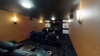 Located at 3151 S Chowen Ave in Minneapolis, MN, this single-level space is purpose-built as a private home theater. The room is designed to replicate an authentic cinema experience, with every detail oriented toward immersive viewing and audio performance.

The interior features a dramatic dark ceiling that absorbs light and enhances on-screen contrast, while textured amber-toned wall panels add warmth and acoustic dampening throughout. Rows of plush black leather reclining chairs with built-in cupholders are arranged in a tiered layout, ensuring clear sightlines to the wall-mounted flat-screen display at the front of the room.

Surround sound speakers are strategically positioned along the walls, supporting a full audio setup. Ambient wall sconces provide soft, theater-style lighting that complements the moody atmosphere without detracting from screen visibility. A geometric-patterned dark carpet covers the floor, reinforcing the cinematic aesthetic.

Additional features include a wall-mounted mini-split HVAC unit for climate control, a small side counter or console table, and framed black-and-white artwork near the entry. The space is accessed through a solid dark door, helping to seal out external light and sound for an optimal viewing environment.