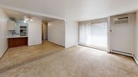 Located at 5634 W Oklahoma Ave in Milwaukee, Wisconsin, this single-floor unit offers a functional and straightforward layout across multiple rooms. The living area is spacious and filled with natural light, courtesy of large windows dressed with vertical blinds that allow sunlight to filter in throughout the day. Soft, neutral-toned carpeting extends throughout the living spaces, creating a cohesive and comfortable feel underfoot. Baseboard heating units are present in the main living and bedroom areas, ensuring efficient warmth during Wisconsin's colder months. The bedroom is well-proportioned and includes a sliding wood-panel closet door, providing practical storage. A standout feature is the generously sized walk-in closet, outfitted with multiple hanging rods and shelving, offering exceptional storage capacity. An additional room visible from the floor plan provides flexible use as a second bedroom or den, also carpeted and connected to closet space. The bathroom is clean and functional, featuring a full soaking tub with a tiled shower surround accented by mosaic tile detail near the top. The overall layout, as seen in the dollhouse floor plan view, is well-organized with clearly defined rooms and straightforward circulation, making the space easy to navigate and practical for everyday living.