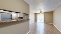 This efficient single-story, one-bedroom, one-bathroom unit is thoughtfully laid out to maximize functionality and comfort throughout. Light wood-style flooring runs continuously across the living spaces, complemented by neutral taupe walls and crisp white trim that create a clean, cohesive aesthetic. The textured ceilings add visual character throughout the unit.

The open-concept kitchen and living area form the heart of the space. The kitchen features white cabinetry, granite-style countertops, a black electric range with overhead ventilation, and a refrigerator, all framed by a half-wall pass-through that connects it to the living room. A ceiling fan with an integrated light fixture serves the living area, which also benefits from a full-height sliding glass door fitted with vertical blinds, allowing natural light to flood in while providing access to outdoor views.

The bedroom is a comfortable, well-lit retreat with its own ceiling fan, a window with blinds for natural light, and a dedicated closet. The full bathroom is well-appointed with a white vanity featuring a granite-style countertop, a full tub-shower combination with tile surround, and light wood-style flooring that ties the space together. A separate closet provides additional storage within the unit.