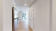 Located at 1810 State Street in San Diego, CA, this single-floor unit offers a clean, modern aesthetic designed to maximize every square foot. The open-concept layout seamlessly connects the kitchen and living area, creating a cohesive and functional living space.

The kitchen is well-appointed with white shaker-style cabinetry, dark stone countertops, a classic white subway tile backsplash, and a full suite of stainless steel appliances including a gas range, microwave, refrigerator, and dishwasher. A deep stainless steel sink with a professional-style faucet adds a refined touch.

The living area is defined by warm, light-toned hardwood-style flooring that runs throughout the entire unit, lending continuity and brightness. A striking wall of floor-to-ceiling windows and a sliding glass door floods the space with natural light and provides views of the surrounding greenery, creating an airy, open ambiance.

A mirrored sliding closet door in the living area further enhances the sense of space and light. The crisp white walls and recessed lighting contribute to the unit's clean, contemporary feel. A louvered interior door adds a subtle architectural detail. The overall design is minimal, bright, and efficiently laid out, ideal for urban living in the heart of San Diego.