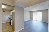 This single-floor residential unit offers a practical and well-appointed layout designed for comfortable everyday living. The spacious living area features warm-toned luxury vinyl plank flooring, neutral beige walls, a textured ceiling, and a sliding glass door fitted with vertical blinds that opens to an outdoor balcony, allowing natural light to fill the room. The kitchen is efficiently designed with white cabinetry, granite-style countertops, stainless steel appliances including a refrigerator and range, and flows seamlessly into the living space via an open pass-through layout. A dedicated laundry area with a full-size washer and dryer is conveniently integrated into the kitchen zone. The two bedrooms are carpeted and each feature ceiling fans with lighting, natural light from window with blinds, and neutral wall tones. The primary bathroom includes a granite-top vanity with an undermount sink, a full tub and shower combination with white tile surround, and a large mirror. A second half-bath provides additional convenience with vinyl plank flooring and clean, minimal fixtures. Throughout the unit, consistent neutral finishes and textured ceilings create a cohesive and move-in ready environment.