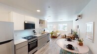 This thoughtfully designed single-floor unit offers a seamless open-plan layout that integrates the kitchen, dining, and living areas into one bright, cohesive space. The modern kitchen is outfitted with two-tone cabinetry — crisp white upper cabinets paired with warm wood-toned lower cabinets — along with stainless steel appliances including a gas range, over-the-range microwave, dishwasher, and full-size refrigerator. A white quartz countertop and open shelving complete the functional yet stylish design. Light wood-look flooring runs throughout the main living area, enhancing the clean, contemporary aesthetic.

The living area is bathed in natural light from large windows overlooking an outdoor courtyard, creating an airy and inviting atmosphere. A dedicated dining space accommodates a round table adjacent to the kitchen for easy everyday living.

The bedroom is generously proportioned and features large sliding glass doors opening directly to a private outdoor patio, filling the room with abundant natural light and providing seamless indoor-outdoor access. Gallery-style wall art adds a personal, curated touch.

The bathroom is clean and bright with light wood flooring, a white vanity, and ample organizational space. A walk-in closet area with built-in shelving is conveniently located nearby, offering practical storage solutions throughout the unit.
