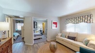 Located at Trails of Sunbrook in Saint Charles, Missouri, this single-floor residence offers a thoughtfully designed layout that balances comfort and functionality. The open floor plan connects the living area to the kitchen and bedrooms, creating a cohesive flow throughout the space.

The living area features warm hardwood-style flooring, neutral-toned walls, and windows dressed with decorative valances that allow natural light to fill the room. The space comfortably accommodates a seating arrangement centered around a woven area rug, lending a relaxed yet inviting atmosphere.

The kitchen is outfitted with rich, dark espresso cabinetry providing generous storage, complemented by light-toned countertops and a full suite of stainless steel appliances, including a refrigerator, electric range, microwave, and dishwasher. A double-basin stainless steel sink and a compact dining area with bar-height seating complete the kitchen space.

Both bedrooms are carpeted and receive natural light through well-positioned windows. One bedroom includes access to a walk-in closet area, while both rooms offer ample space for furnishings. The bathroom features a clean, bright design with a shower-tub combination, wood-style flooring, and a crisp white finish throughout. The overall ambiance is warm, modern, and move-in ready.